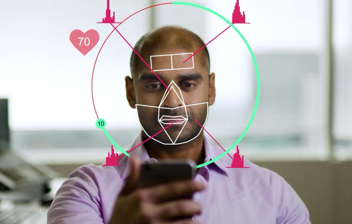 Man houdt smartphone vast; gezichtsherkenning met scanraster en cirkeloverlay.