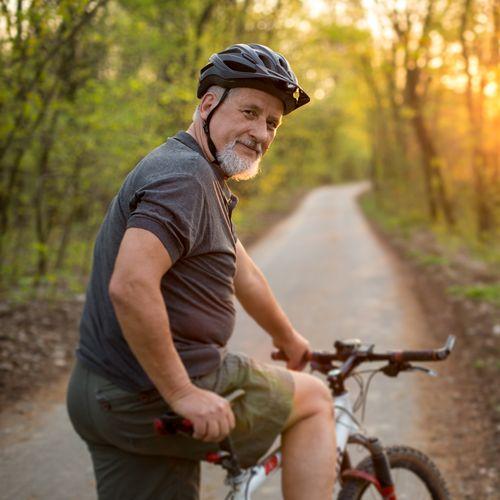 Man op mountainbike op bospad bij zonsondergang, kijkt lachend naar de camera.